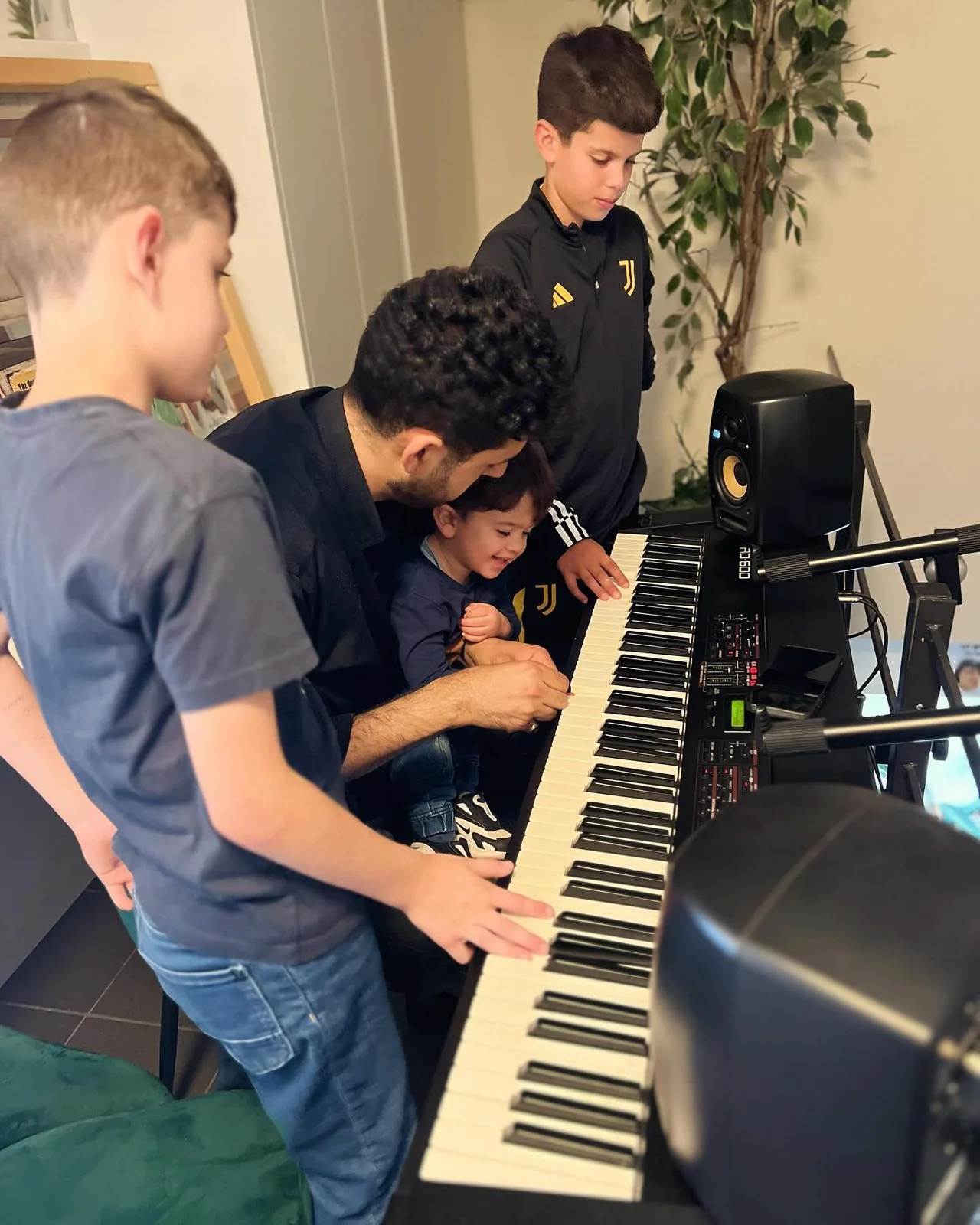 Kinderen staan samen bij een keyboard terwijl een deelnemer de toetsen bespeelt.